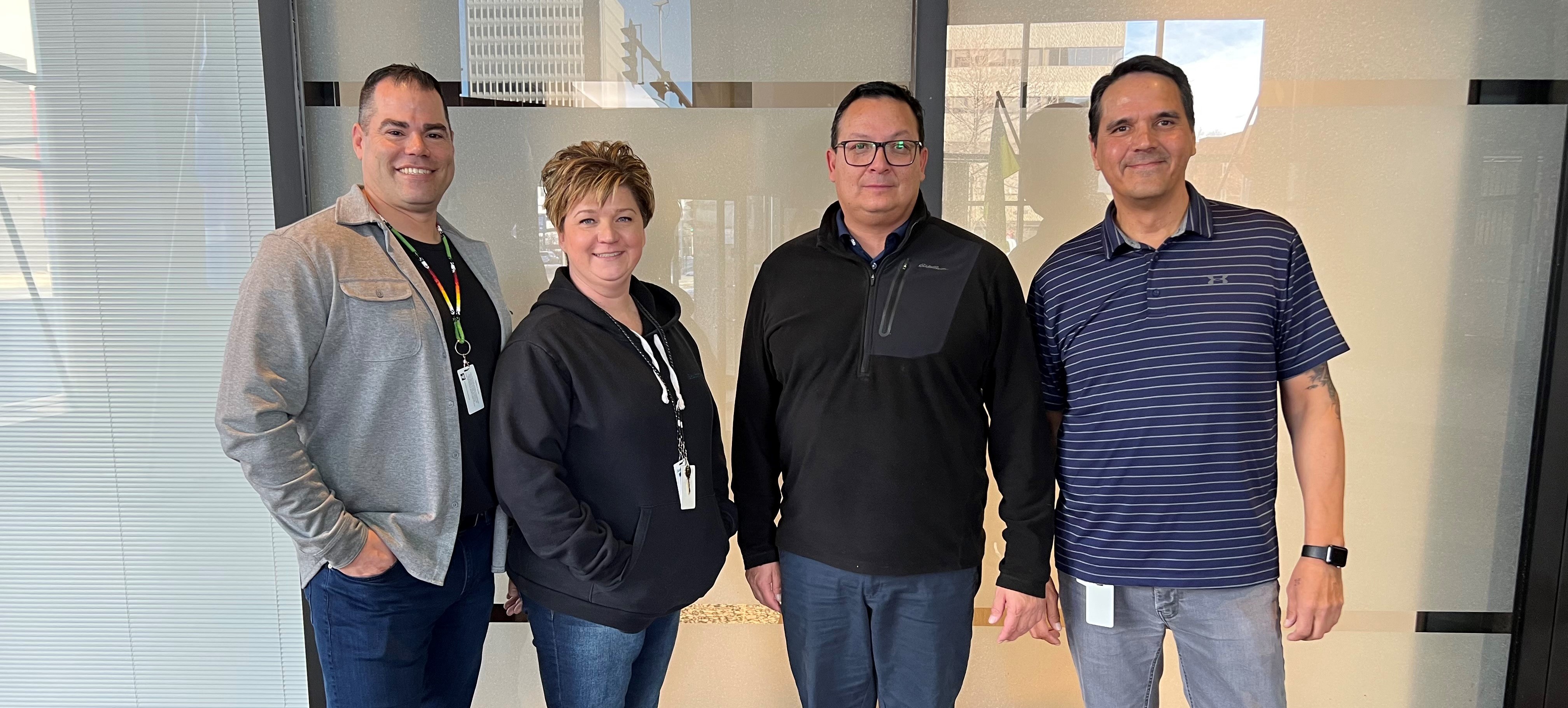 Four people stand in front of office windows.
