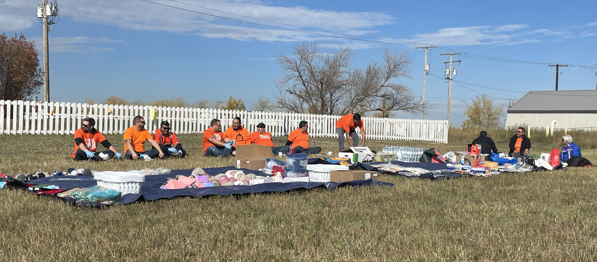 Two tarps containing food and household items are laid out in a field.