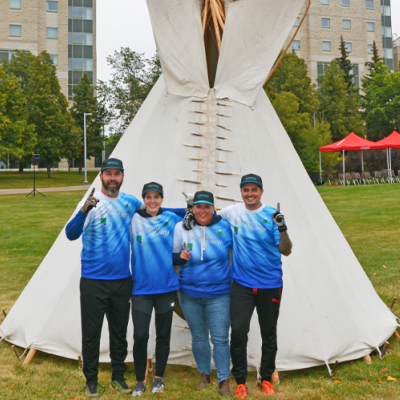 Four employees wearing matching blue shirts stand in front of the tipi they built. 
