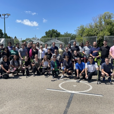 A group of people pose on a concrete surface, each holding lacrosse sticks.