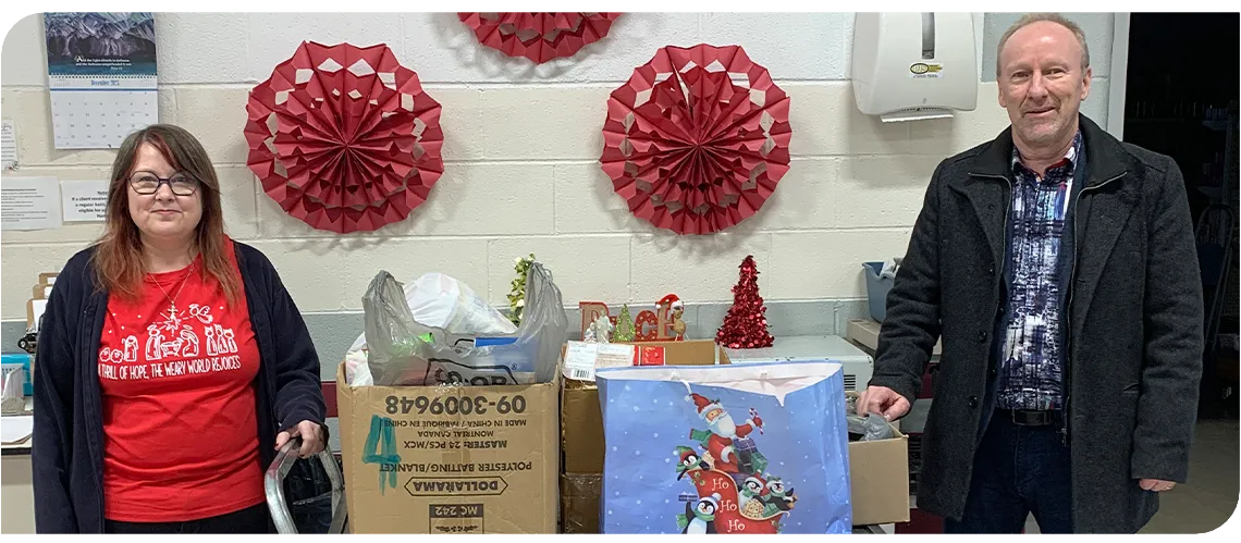 Two people stand on either side of a cart full of bags and boxes of donated food items. 