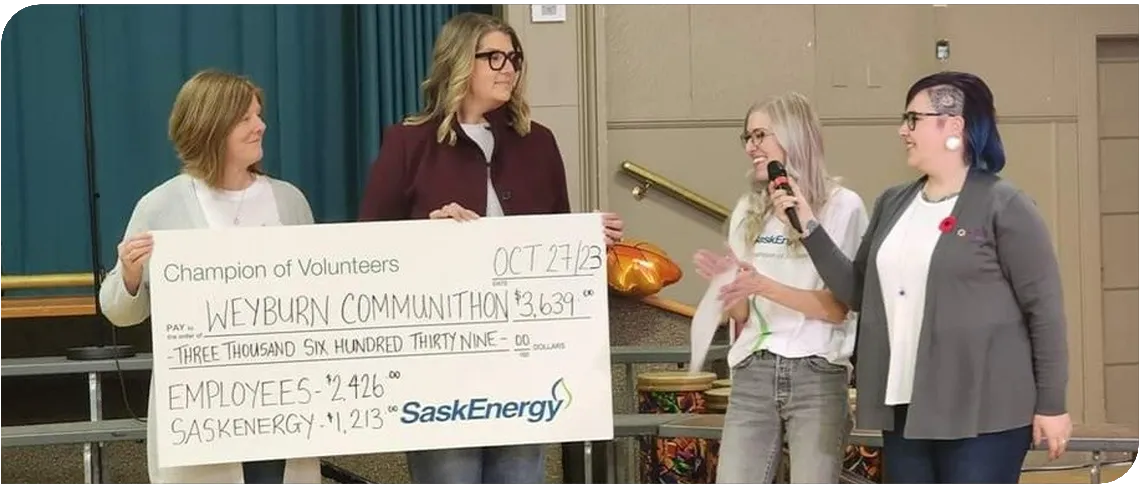 Two people hold a giant novelty cheque, while a person holds a microphone to another person's mouth.