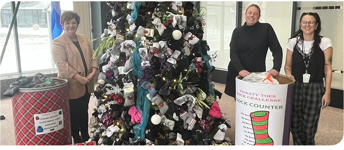 Three people stand in front of a Christmas tree
