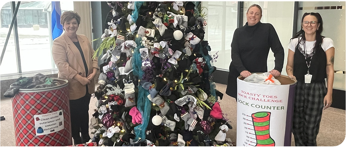 Three people stand in front of a Christmas tree